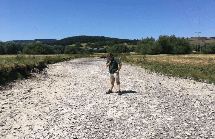 A man inspects a dry riverbed